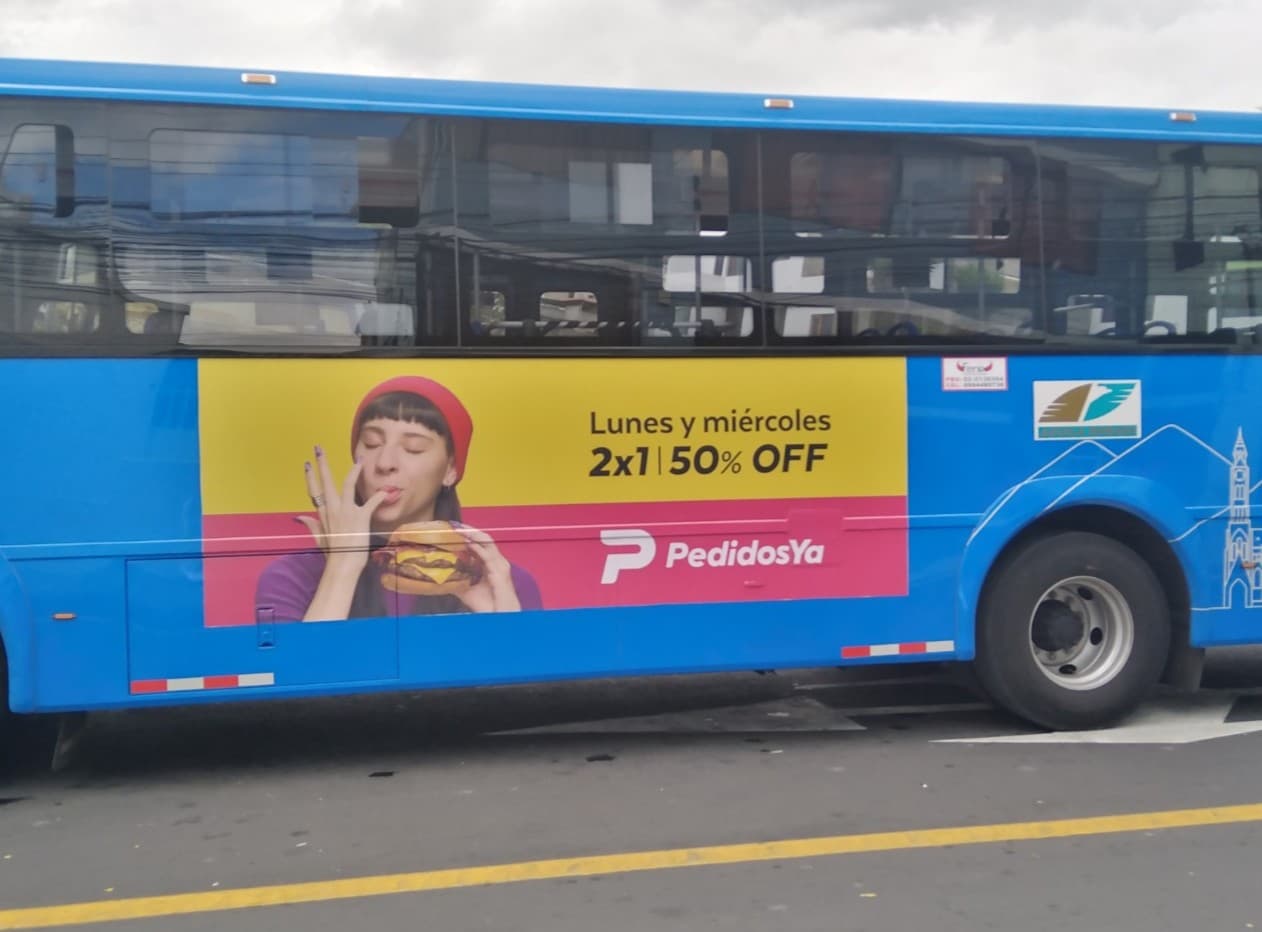 Publicidad lateral de PedidosYa en bus azul, promoción de beneficios 2x1